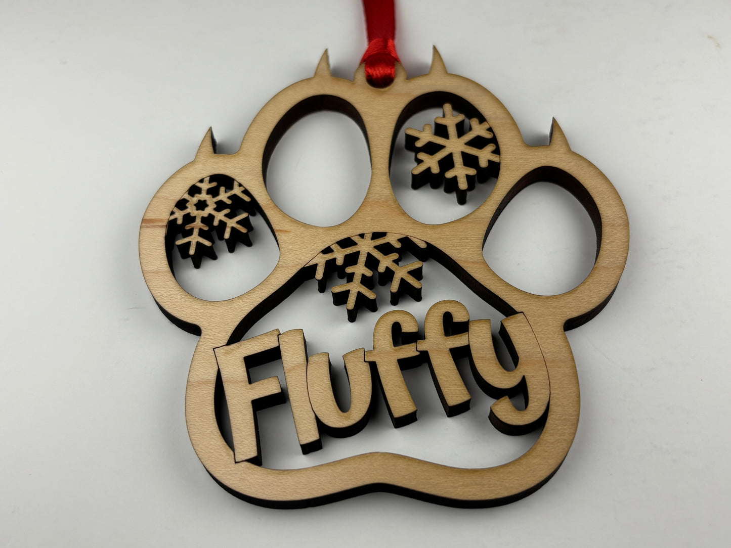 Wooden ornament shaped like a paw with 'Fluffy' and snowflake designs on a white background