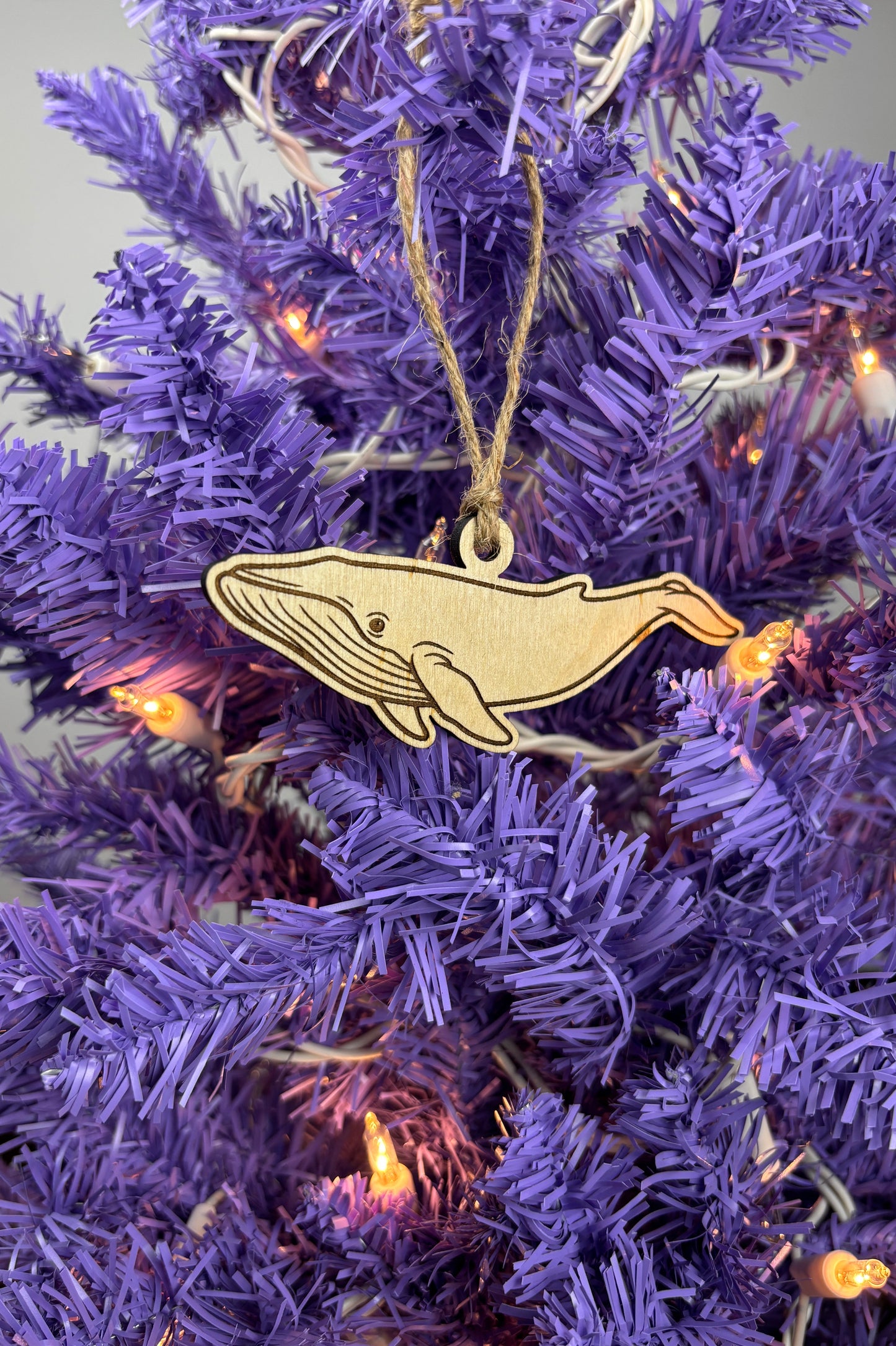 Decorative whale ornament on a purple Christmas tree with lights.