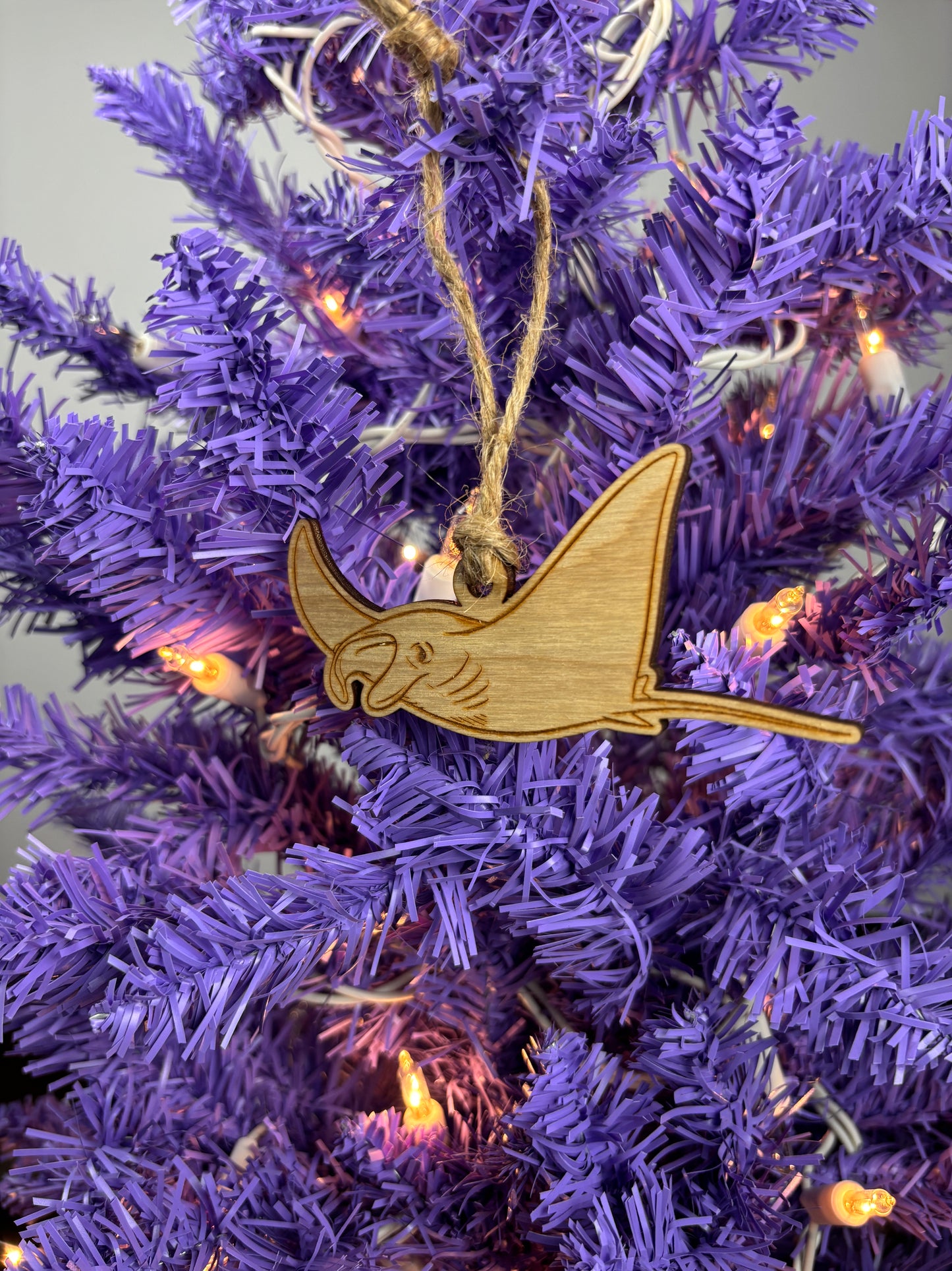 Wooden Manta ray ornament hanging on a purple Christmas tree with lights.