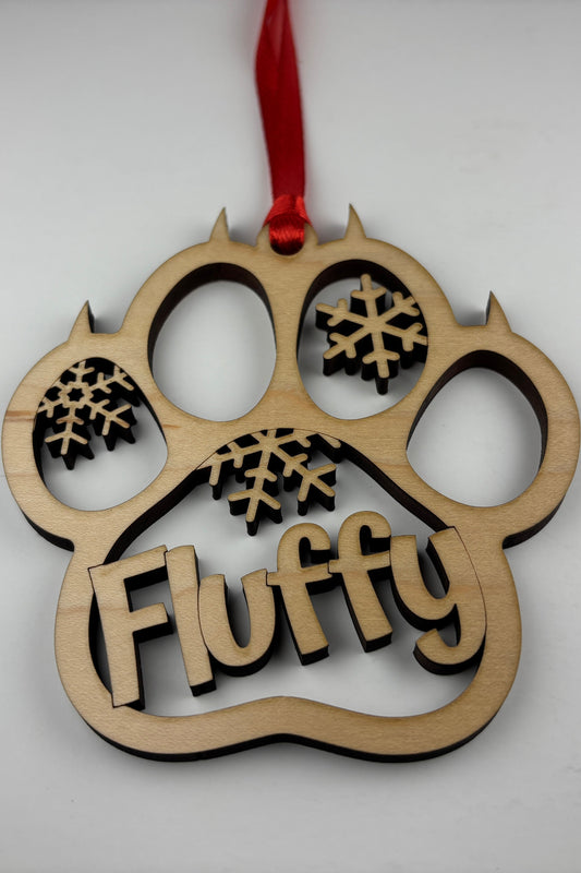 Wooden ornament shaped like a paw with 'Fluffy' text and snowflake designs, hanging on a red ribbon against a white background.