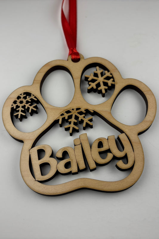 Wooden ornament shaped like a paw print with 'Bailey' and snowflakes on a white background