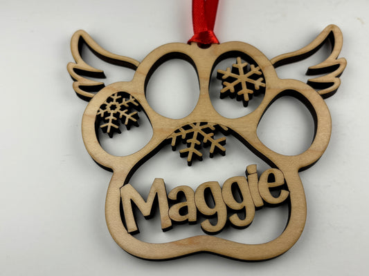 Wooden ornament shaped like a paw print with snowflakes and the name 'Maggie' on a white background.