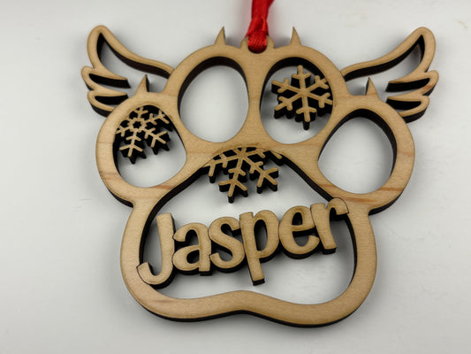 Wooden ornament shaped like a paw with 'Jasper' and snowflake designs on a white background