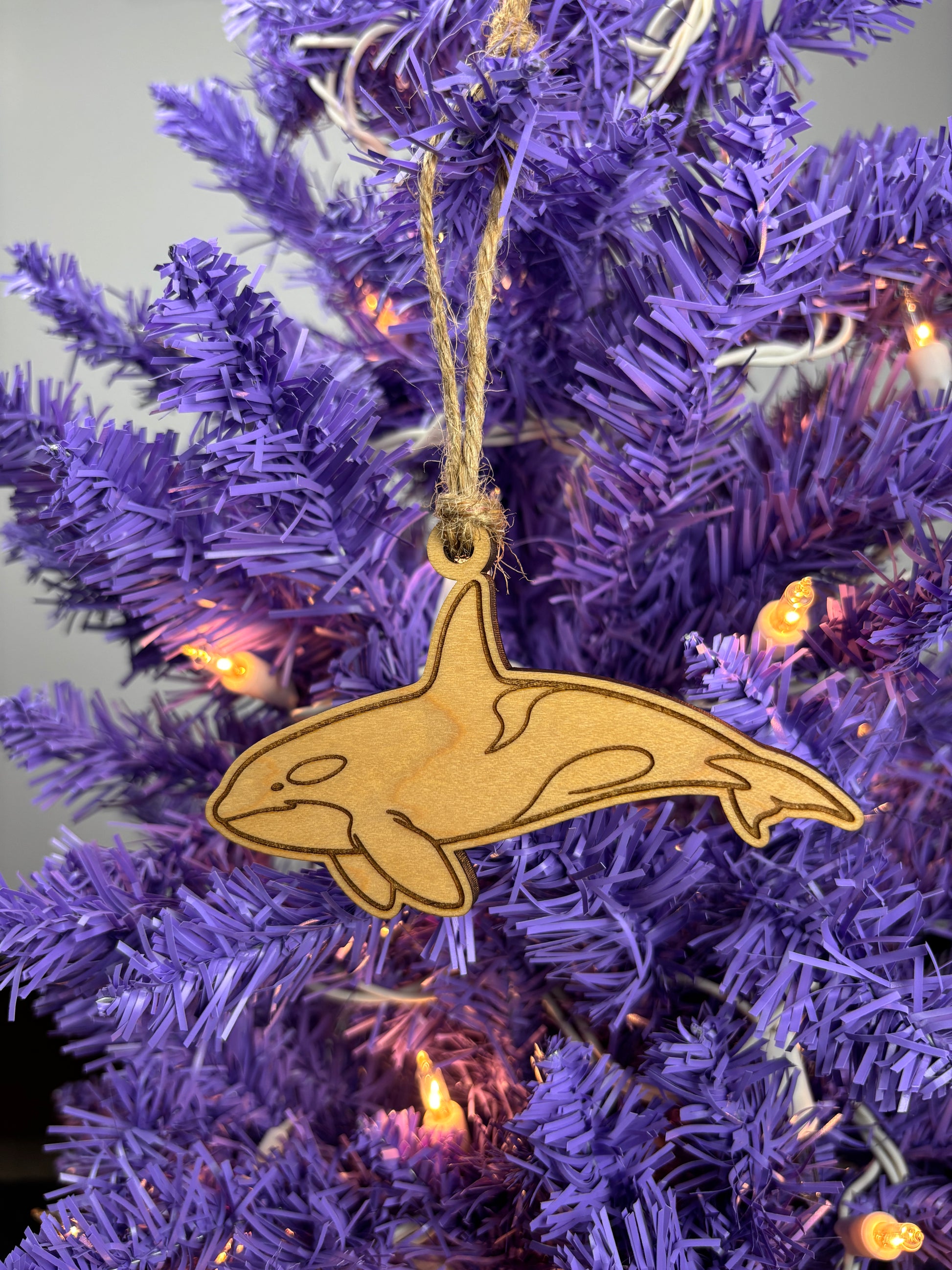 Wooden orca whale ornament hanging on a purple Christmas tree.