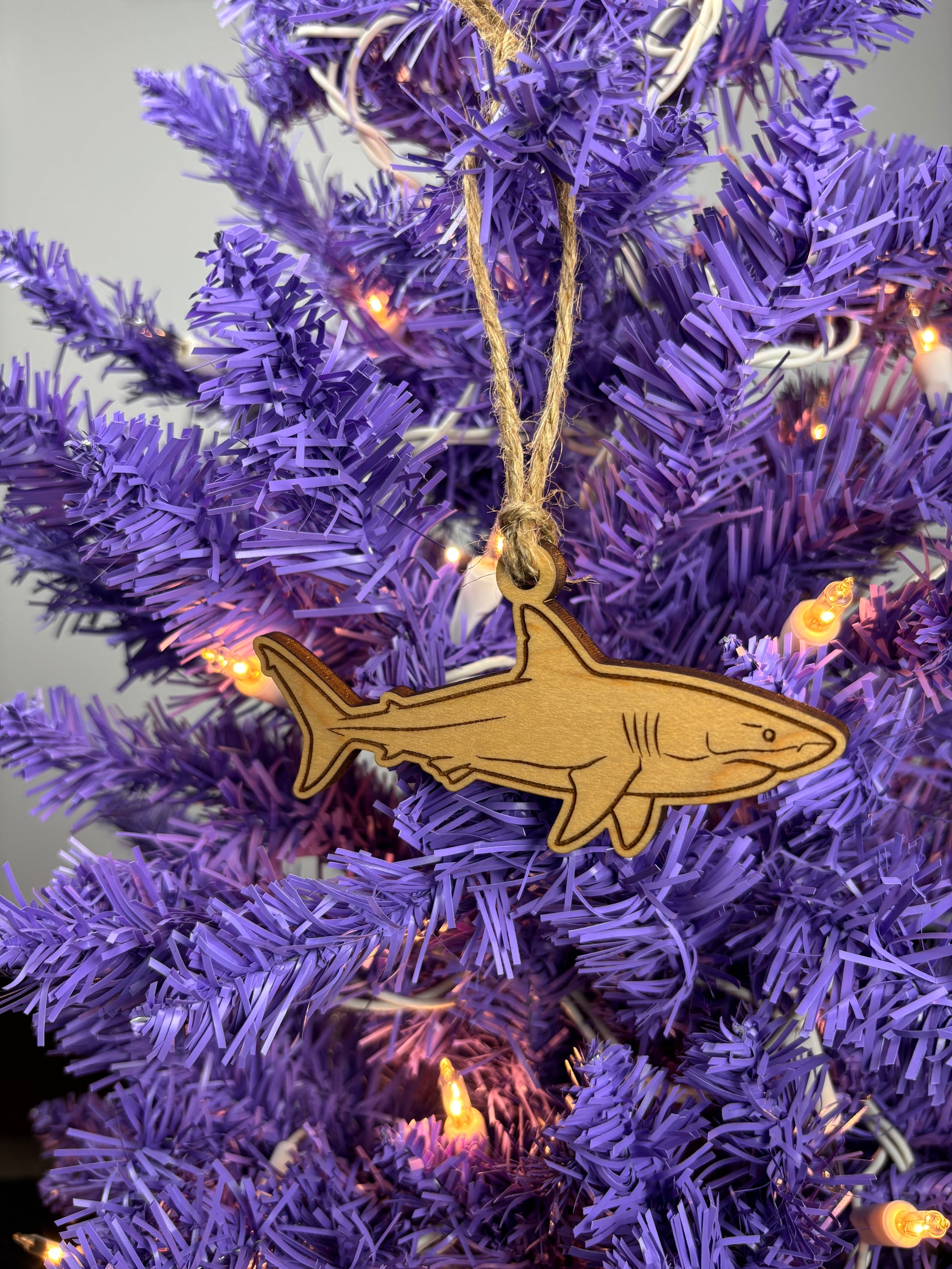 Shark ornament hanging on a purple Christmas tree with lights.