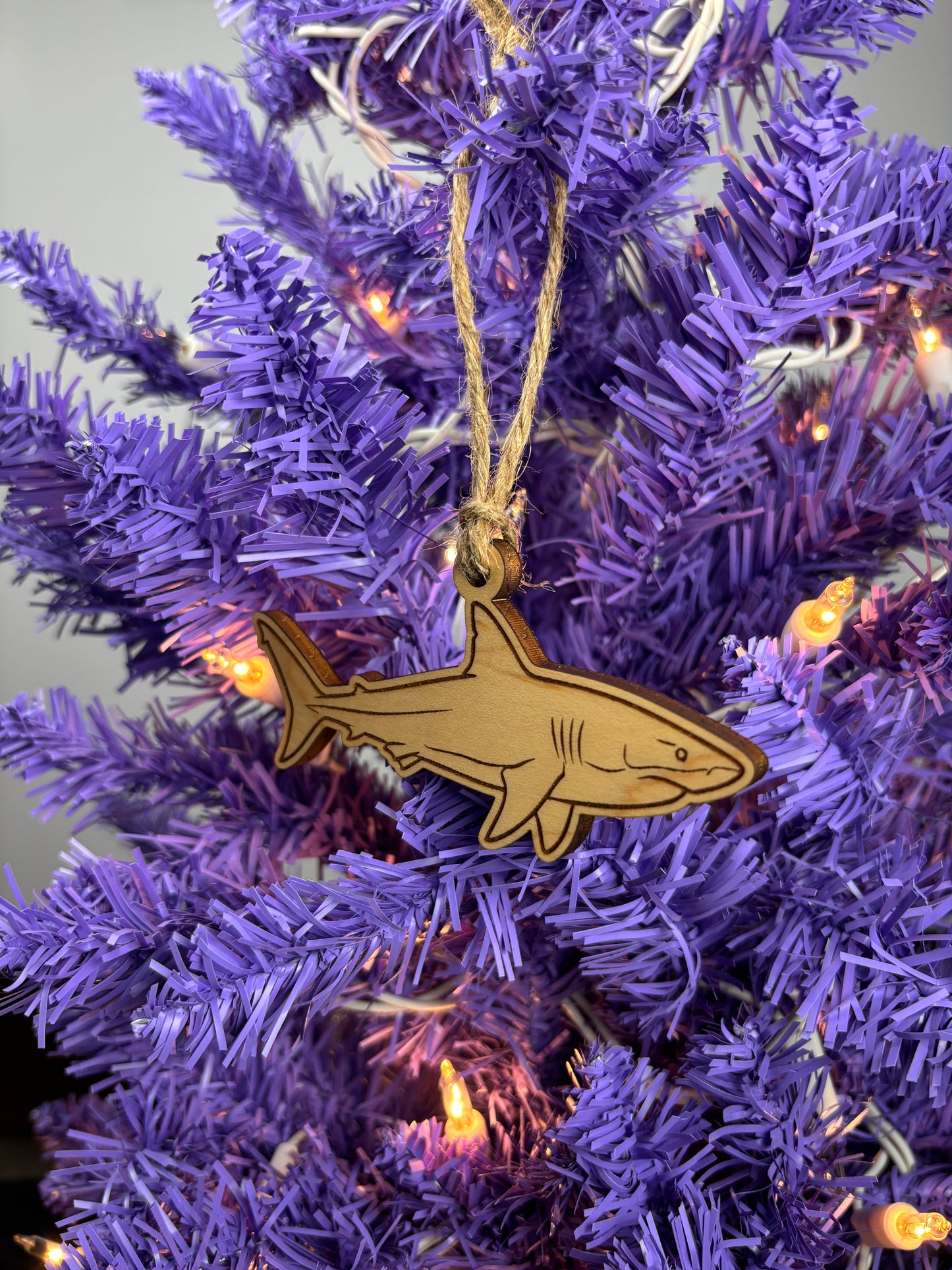Shark ornament hanging on a purple Christmas tree with lights.